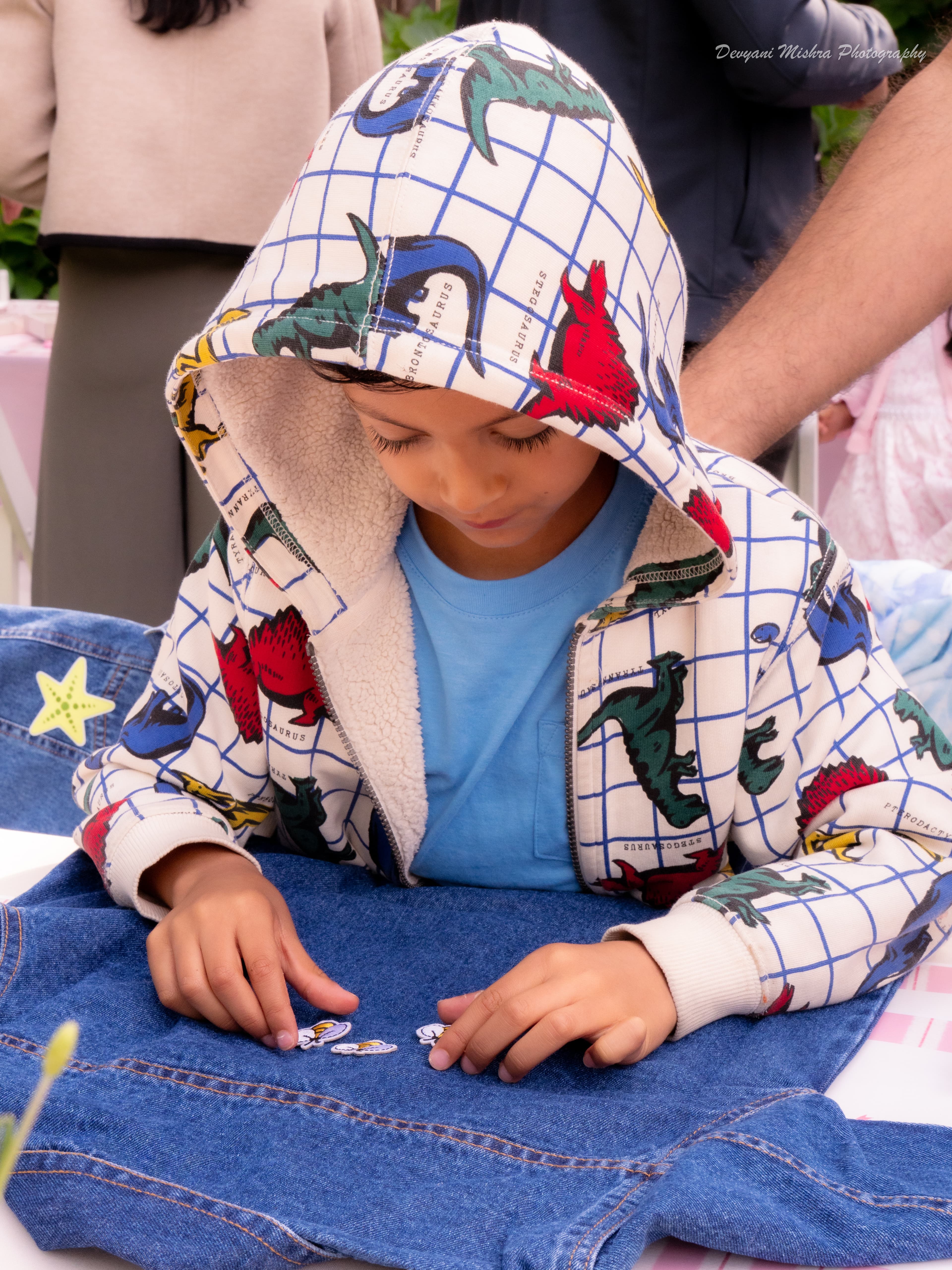 Young kid in dinosaur print jacket carefully placing patches on a denim jacket