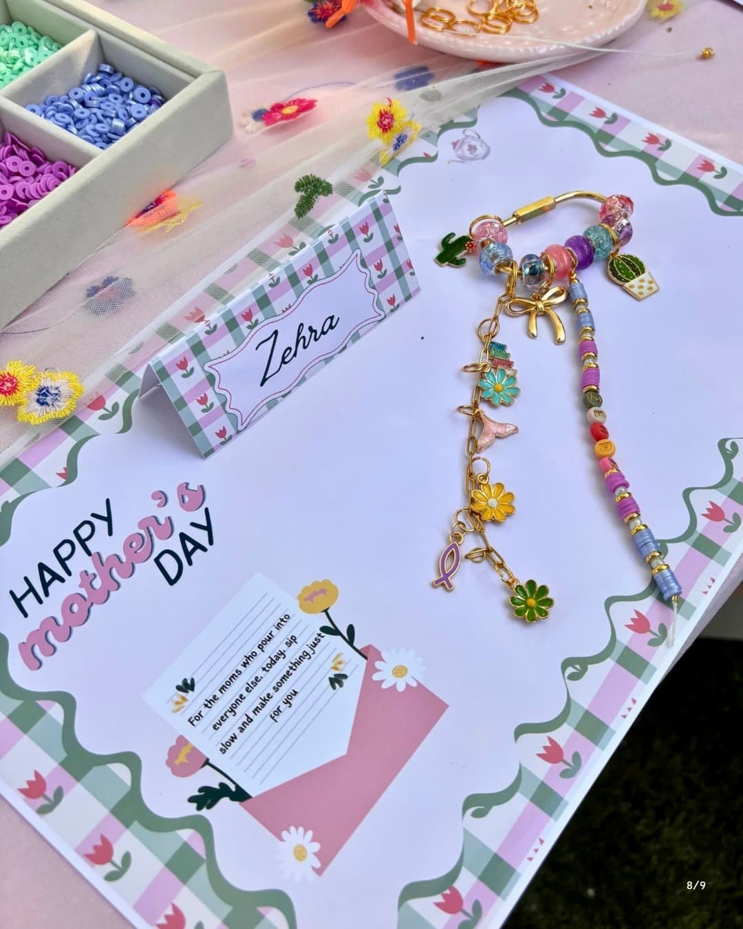 Finished charm bracelet on Mother's Day mat — gold chain with cactus, butterfly and flower charms, all guest-selected